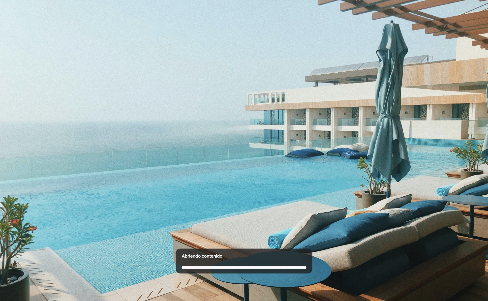 Estado de carga sobre una foto de la piscina de un hotel, con el mensaje 'Abriendo contenido' y una barra de progreso